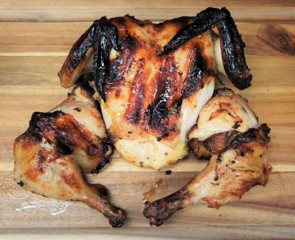 A whole grilled chicken that was marinaded for 24 Hours in a mojo marinade displayed on a wood cutting board