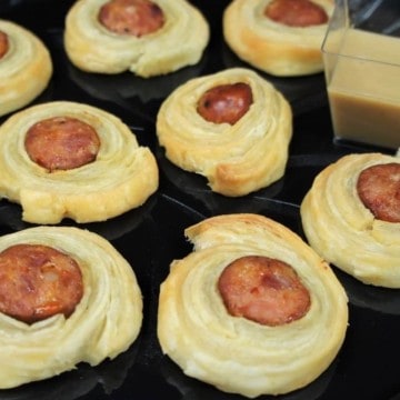 Andouille Sausage Puffs sliced sausage wrapped in puff pastry arranged on a black platter and served with a mustard sauce on the side