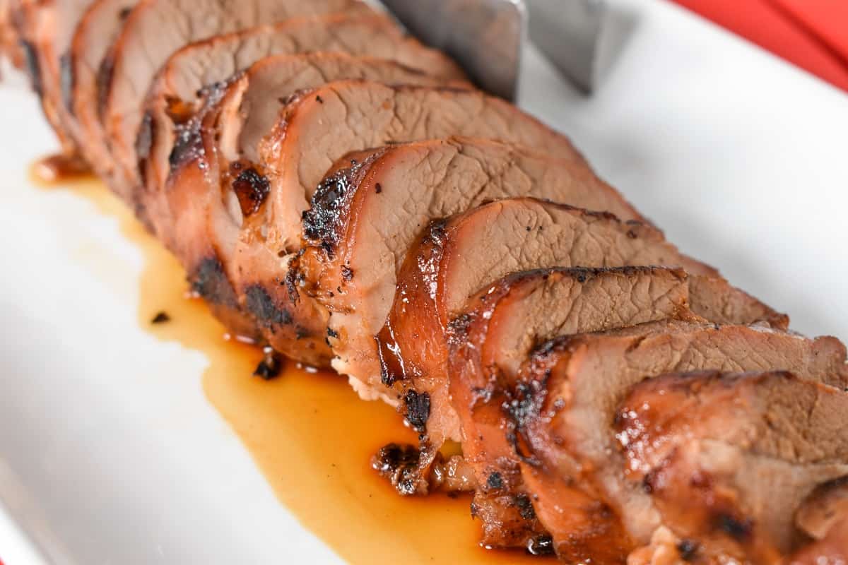 Asian marinated pork tenderloin sliced into thin pieces and served on a white platter.