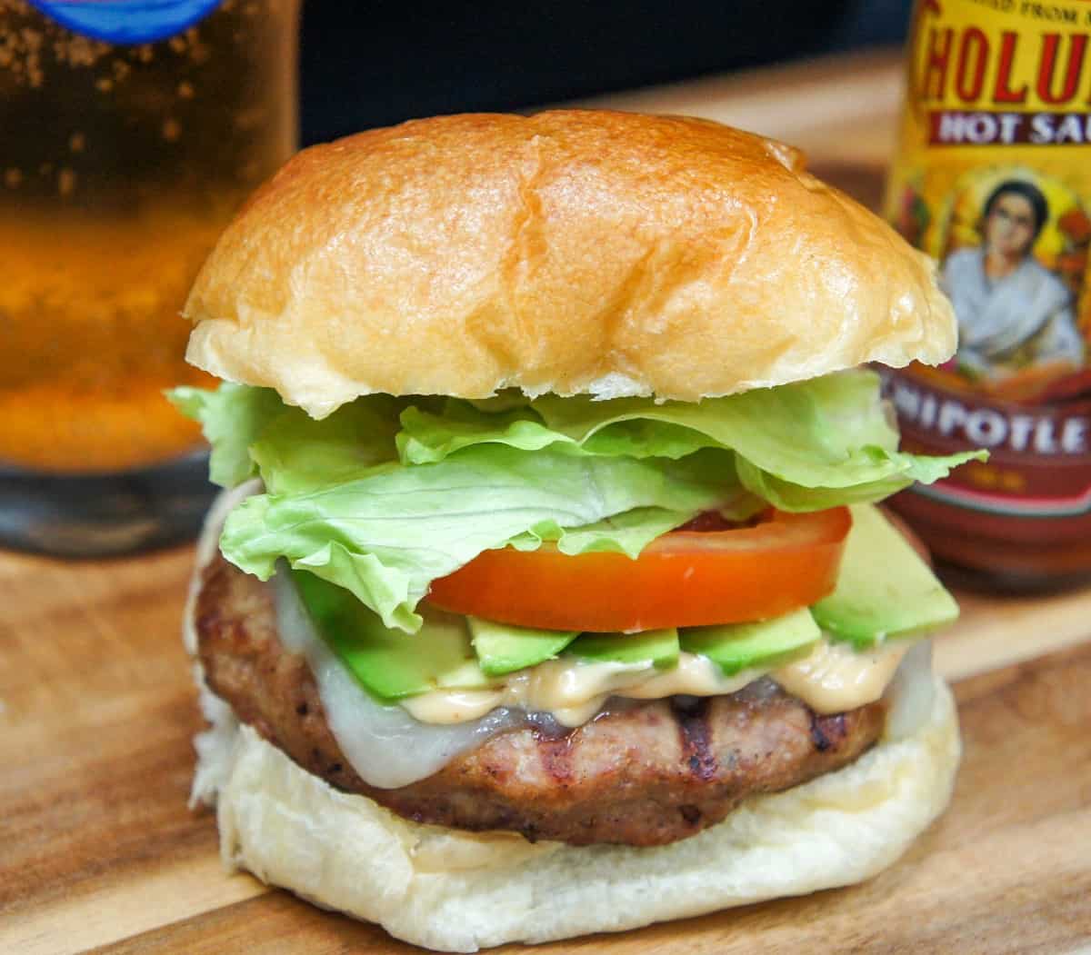 A close up of the finished burger with a glass of beer and hot sauce in the background.