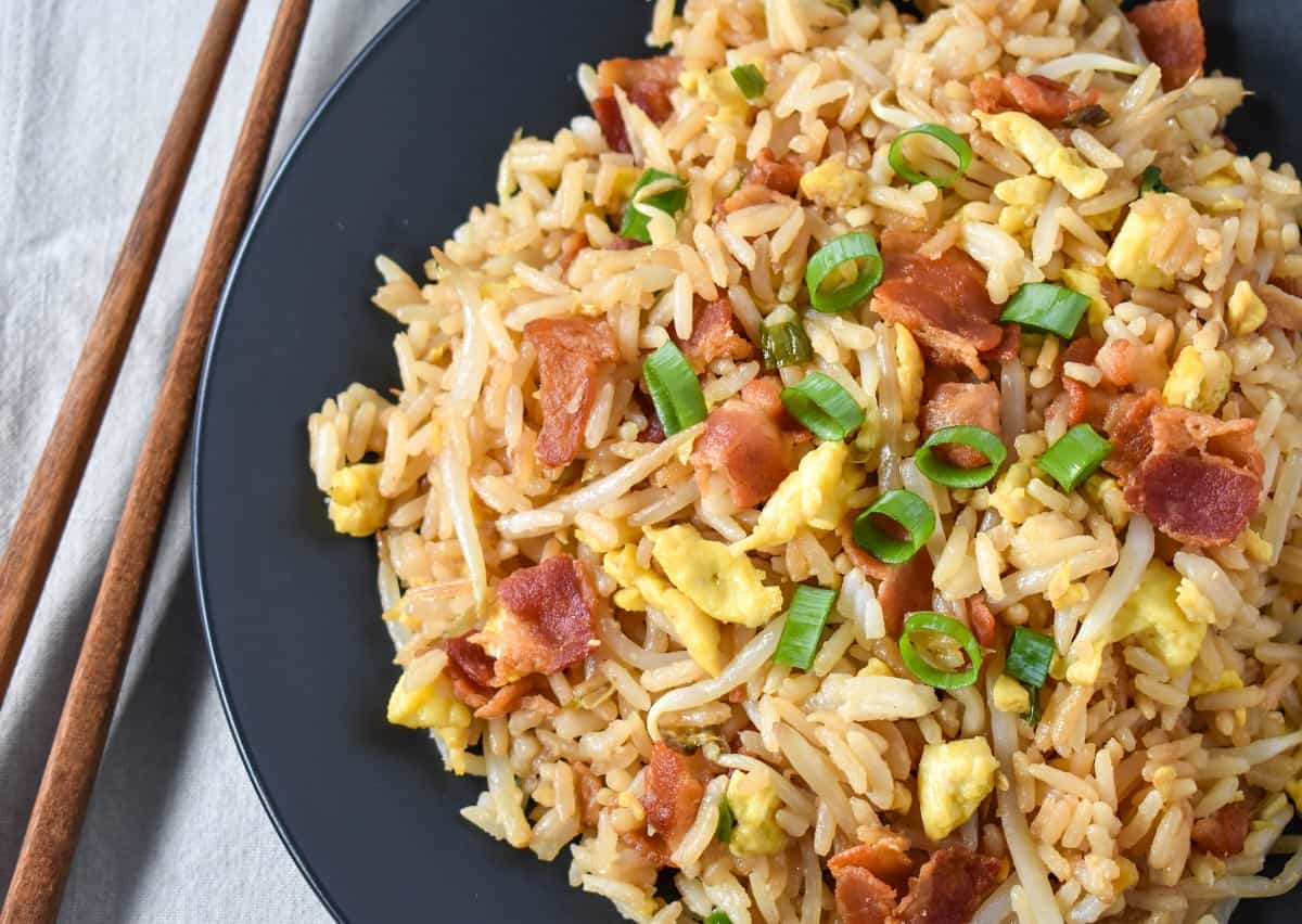 A close up of the fried rice served on a black plate with chopsticks to the left side.