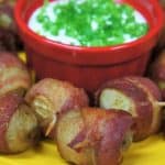 Bacon Potato Bites small potatoes wrapped in crispy bacon, secured with a toothpick served with a side of sour cream garnished with green onions
