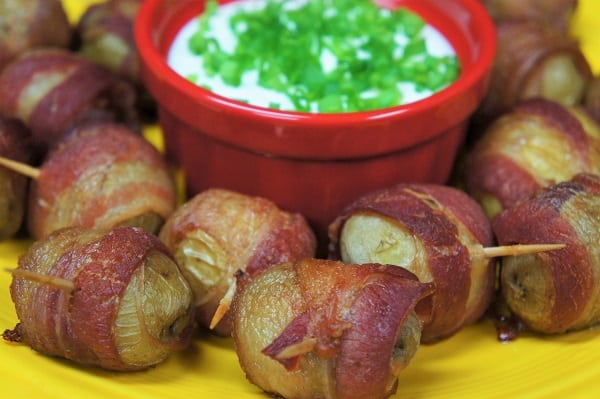Bacon Potato Bites small potatoes wrapped in crispy bacon, secured with a toothpick served with a side of sour cream garnished with green onions
