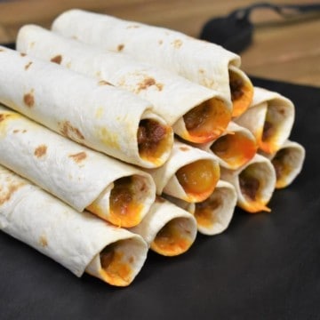 Beef Taquitos stacked on a black cutting board