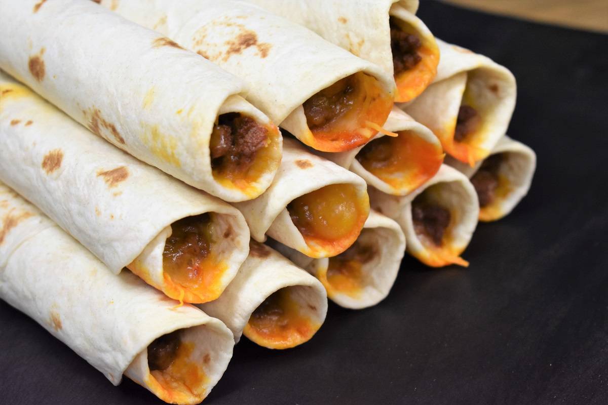 A close up of beef taquitos stacked on a black cutting board