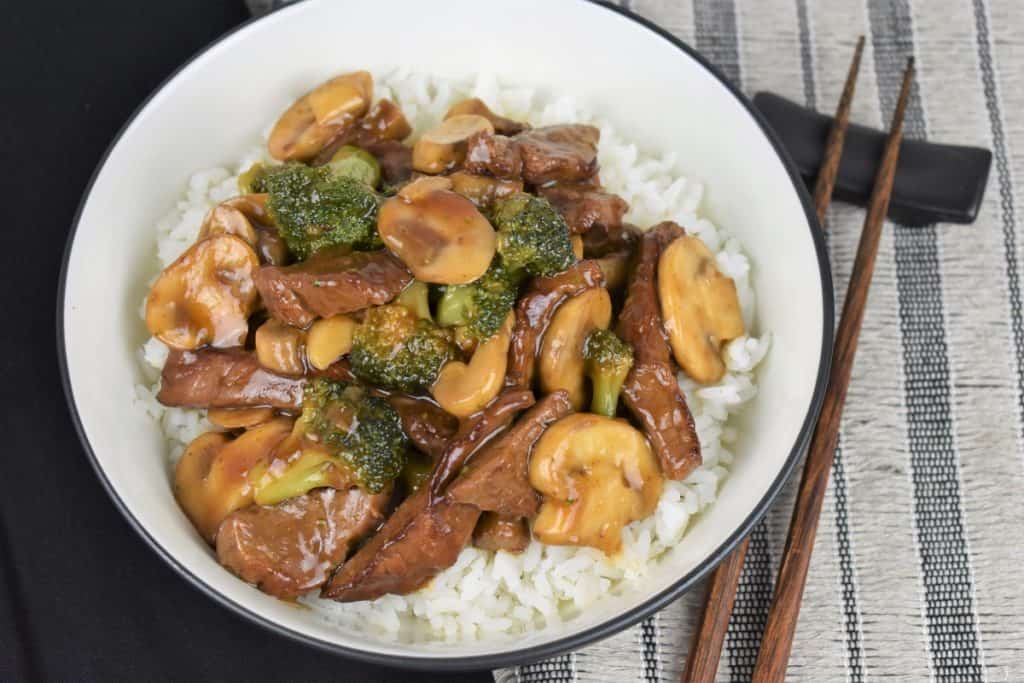 Beef and Broccoli served over white rice in a white bowl with chop sticks on the side