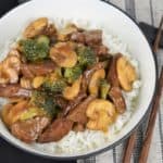 Beef and Broccoli served over white rice in a white bowl with chop sticks on the side