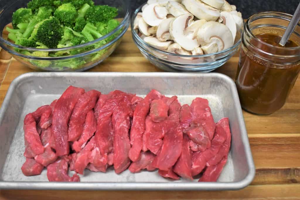 Beef and Broccoli Prep, sliced beef, mushrooms, broccoli and Asian sauce displayed on a cutting board prior to cooking