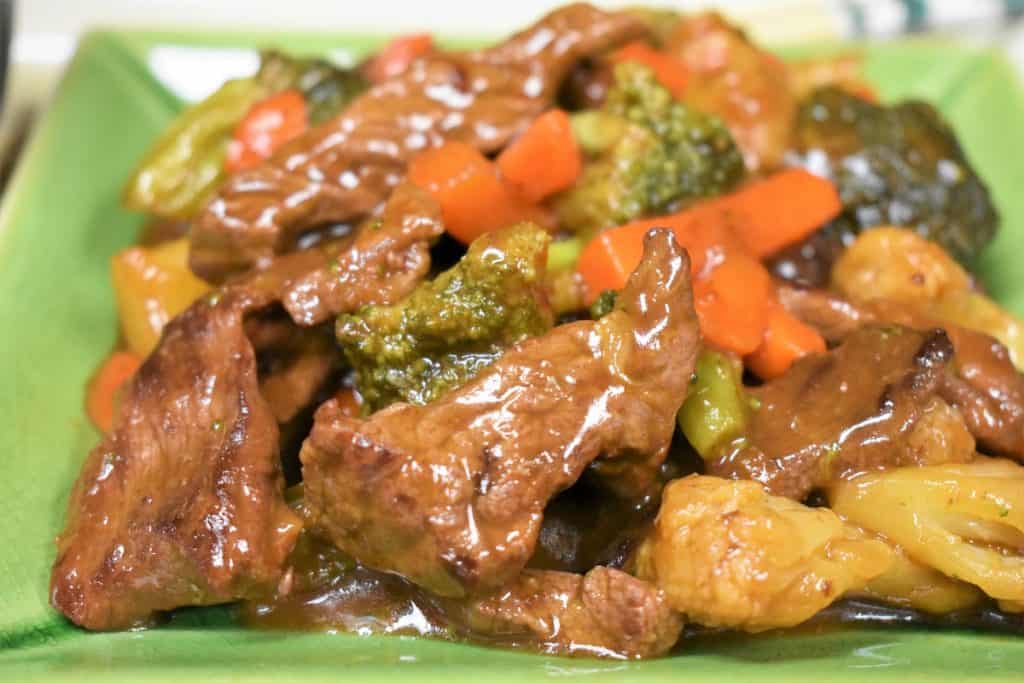 A close up of beef and vegetable stir fry served on a green plate.