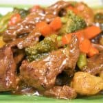 A close up of beef and vegetable stir fry served on a green plate.