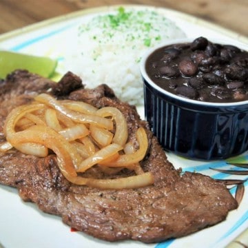 Bistec de Palomilla, thin sirloin steak served with cooked onions, white rice and black beans