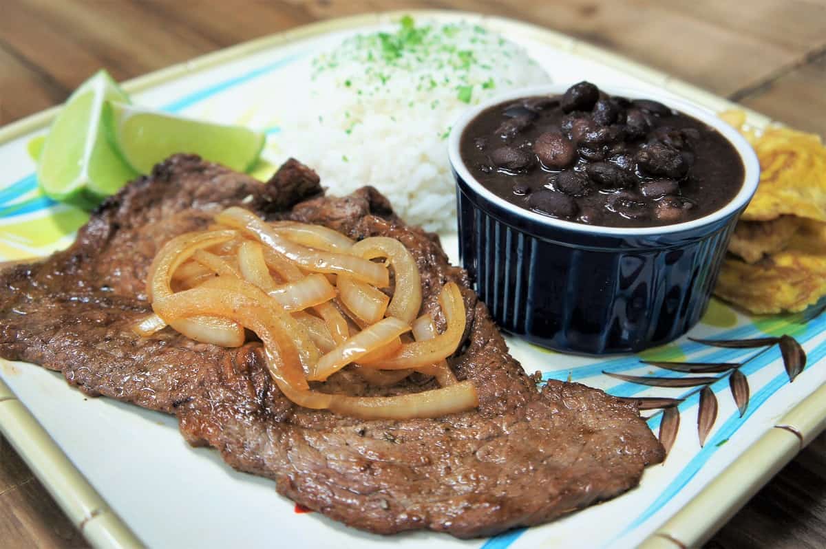 Bistec de Palomilla, thin sirloin steak served with cooked onions, white rice and black beans