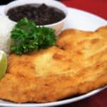 Breaded chicken steak, a thin chicken cutlet that is breaded and fried, served with white rice and black beans on a white plate.