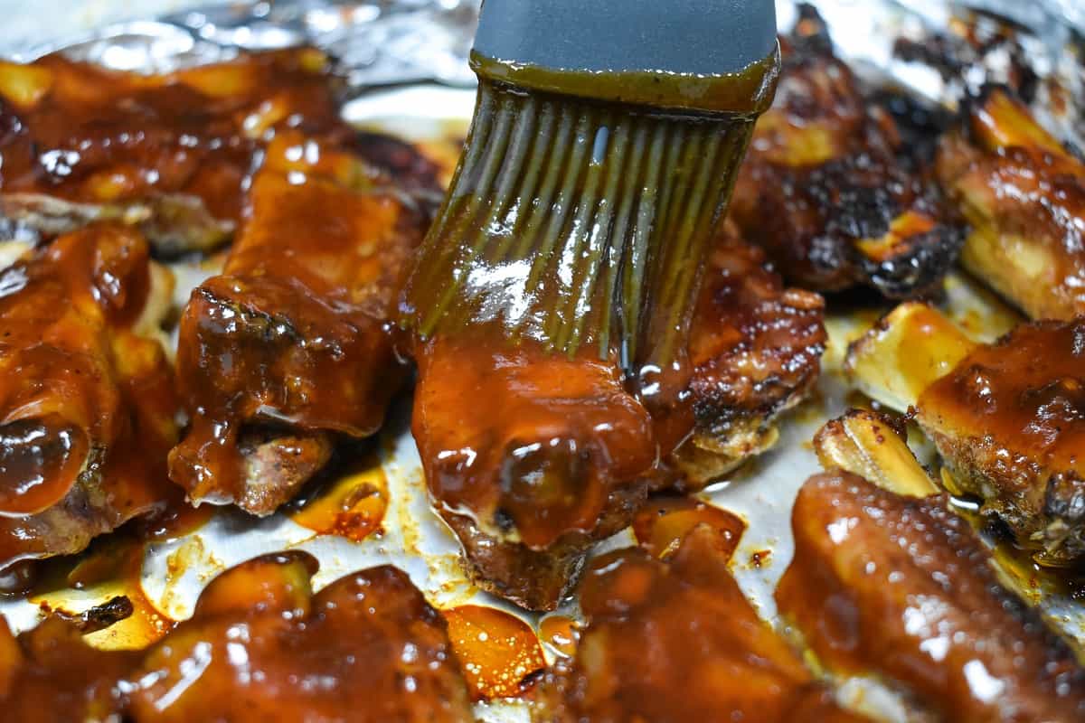 Little ribs being coated with barbecue sauce with a pastry brush.