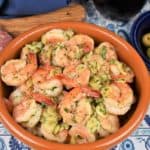 Camarones al Ajillo garlic shrimp in a red clay bowl with olives, cheese and salami displayed in plates on the side