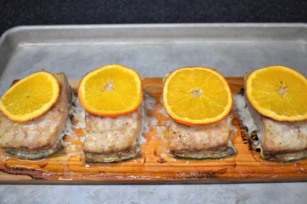 Four pieces of Mahi mahi on a cedar plank, each with a thin orange slice on top.