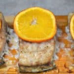 Three pieces of Mahi mahi on a cedar plank with a thin orange slice on top.