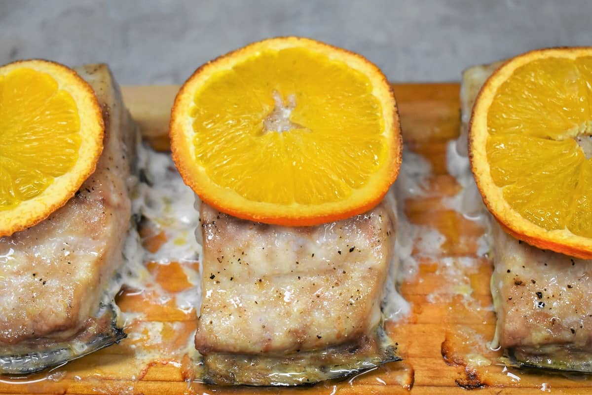 Three pieces of Mahi mahi on a cedar plank with a thin orange slice on top.