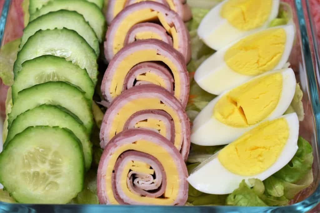 A close up of cucumber slices, ham, turkey and cheese roll-ups and a quartered hard boiled egg
