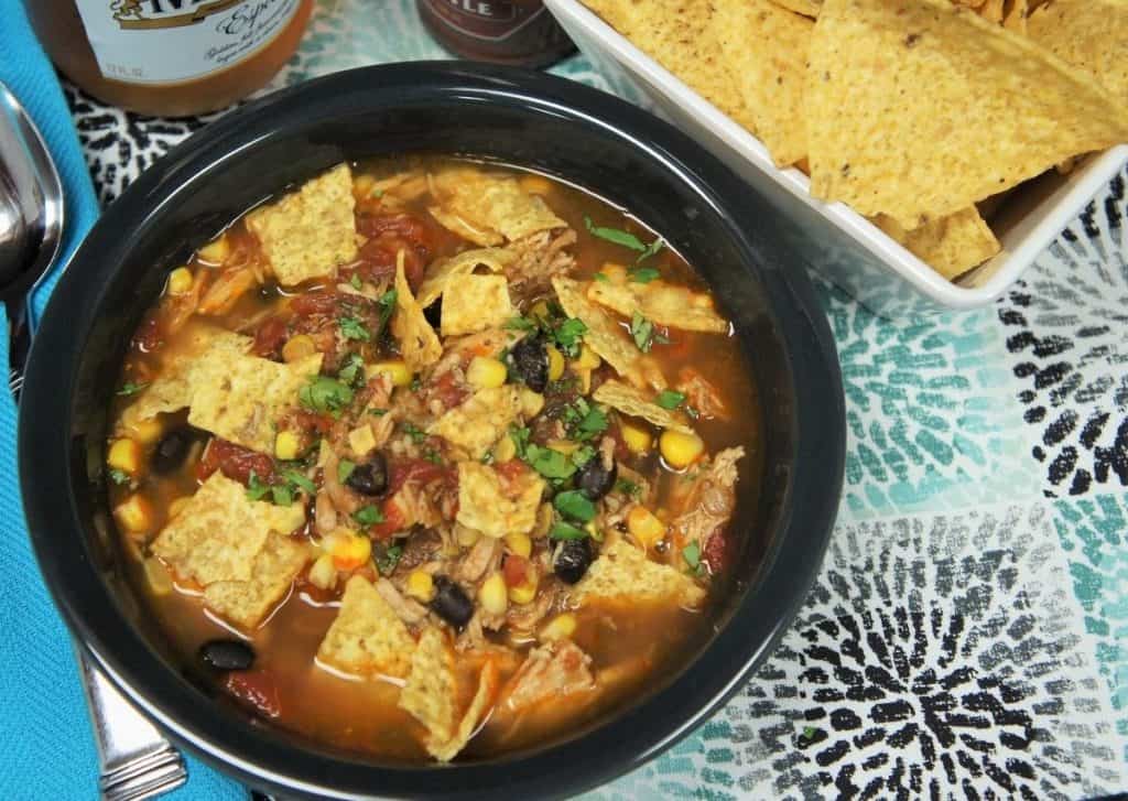 Chicken corn tortilla soup black beans, corn, shredded chicken in a light tomato broth served in a gray bowl with corn chips, beer and hot sauce on the side