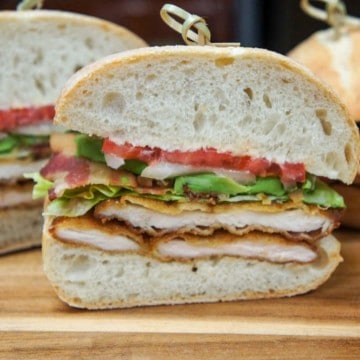 The sandwich, cut in half and displayed on a wood cutting board.