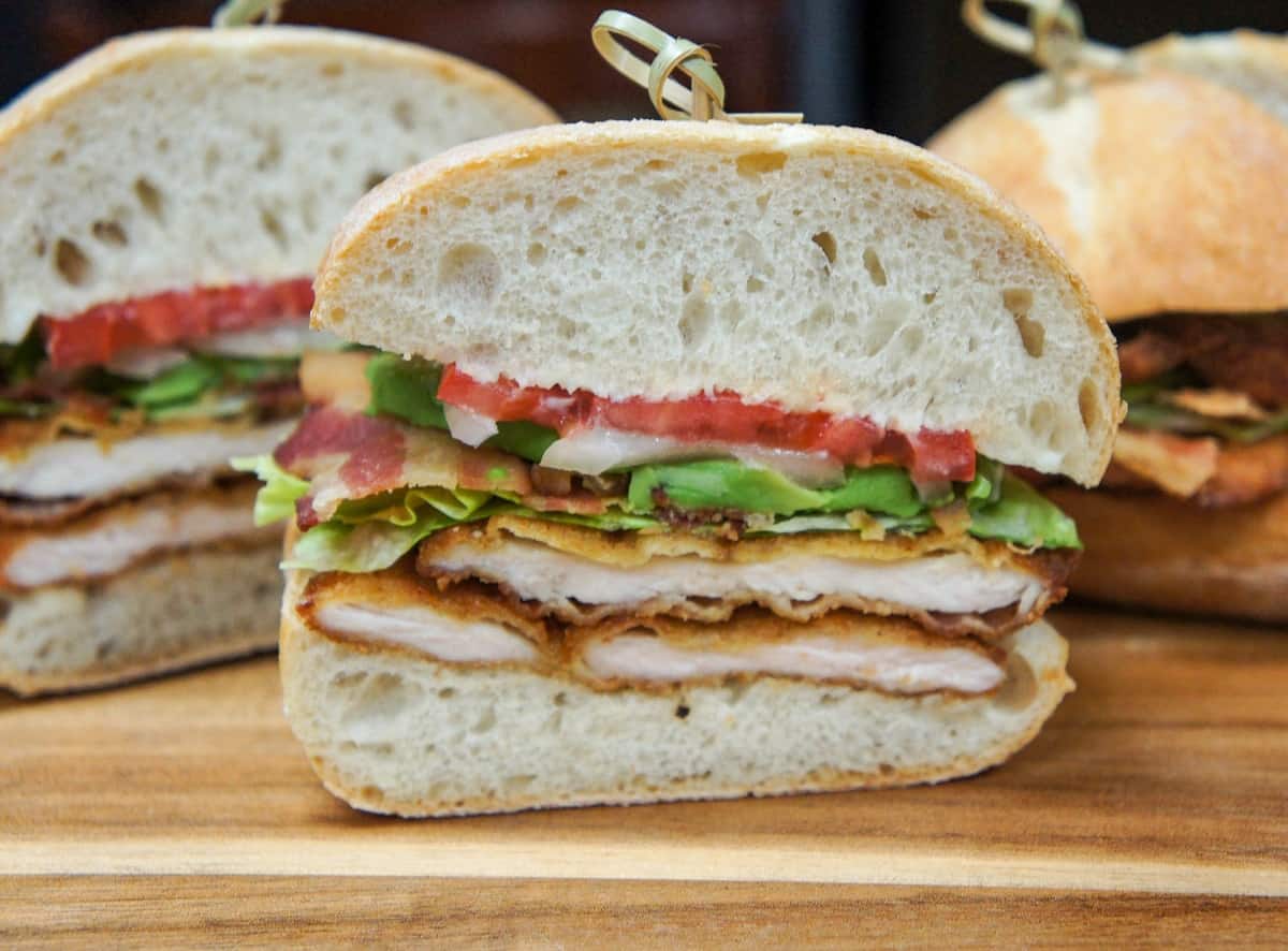 The sandwich, cut in half and displayed on a wood cutting board.