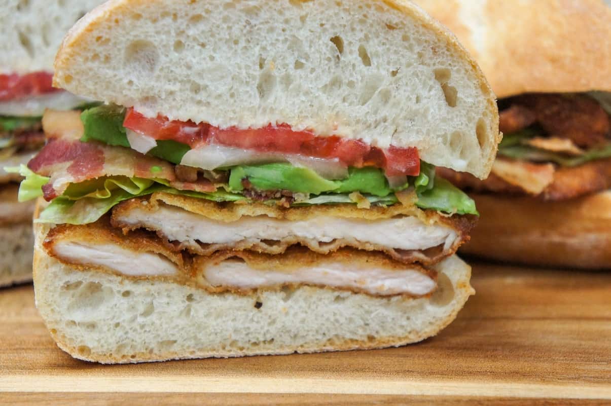 A close up image of the chicken cutlet sandwich half, displayed on a wood cutting board.