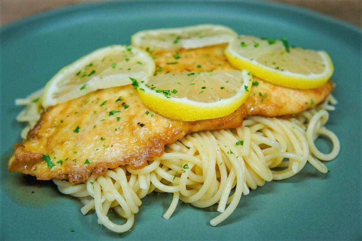 Chicken Francaise on a bed o spaghetti, served on a green plate.