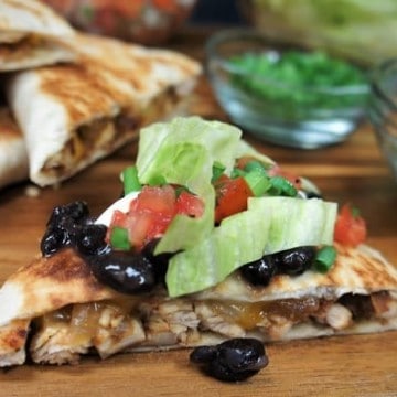 Chicken Quesadillas cut into triangles and topped with lettuce, tomatoes and black beans served on a wood cutting board