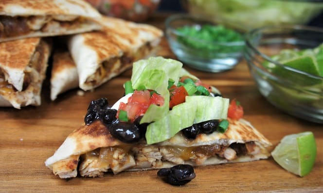 Chicken Quesadillas cut into triangles and topped with lettuce, tomatoes and black beans served on a wood cutting board