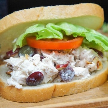 Chicken salad on sliced white bread topped with lettuce and tomato slice with pickle spears and chips on the side.