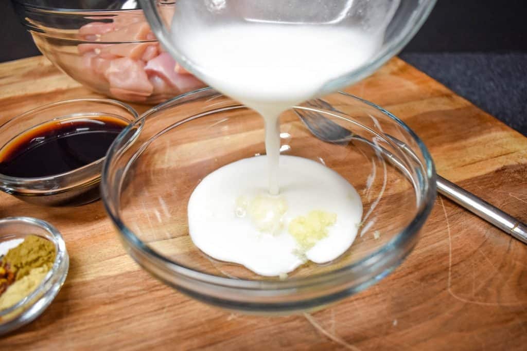 Coconut milk being added to a large, clear glass bowl.