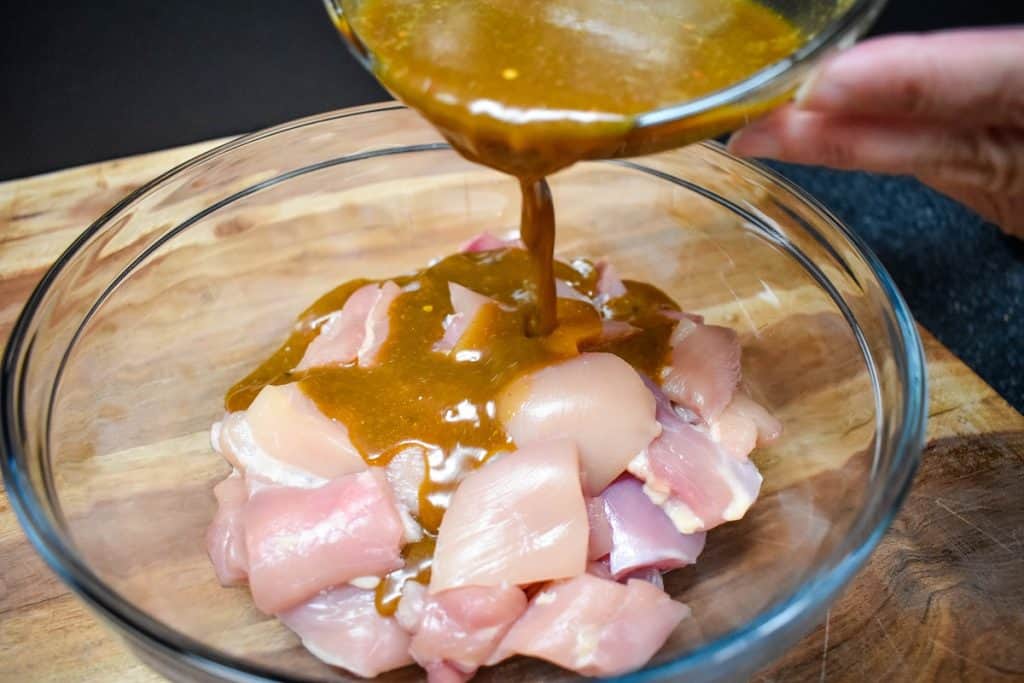 Marinade being added to raw chicken thighs that are cut into pieces.