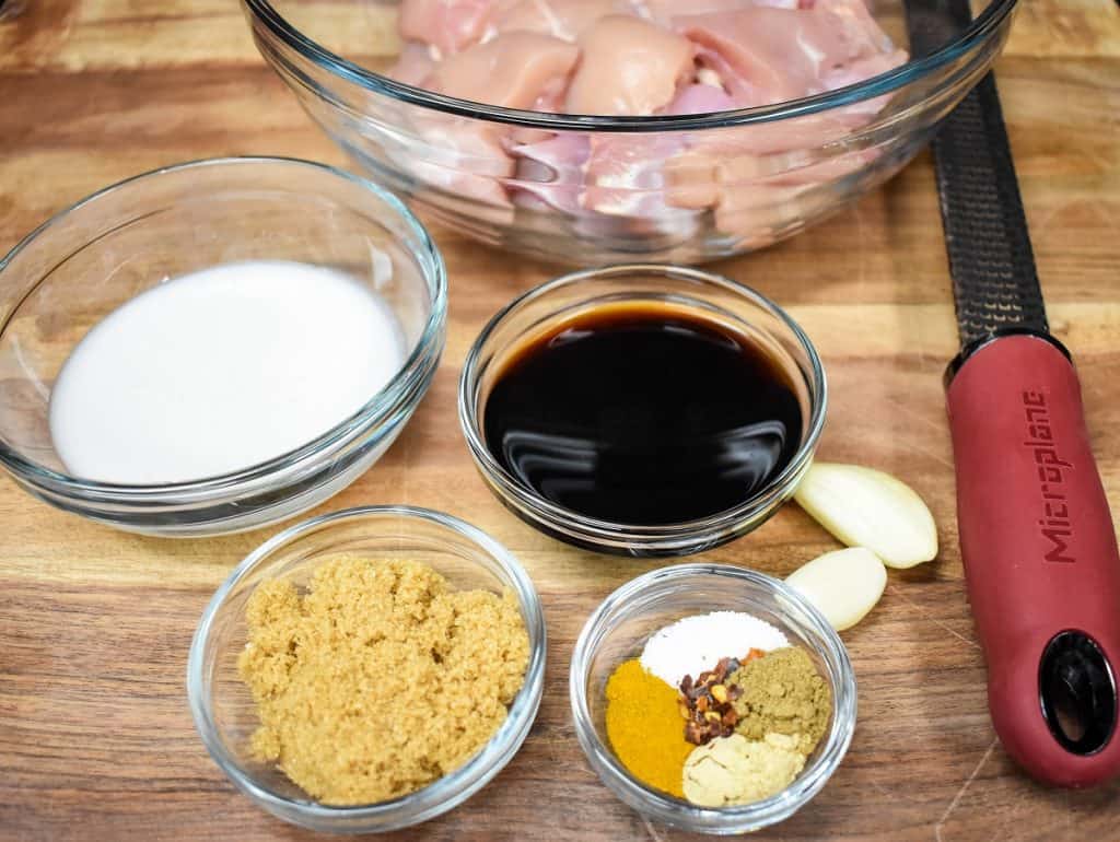 The ingredients for the chicken satay, before cooking. Set up in clear glass bowls and displayed on a wood cutting board.