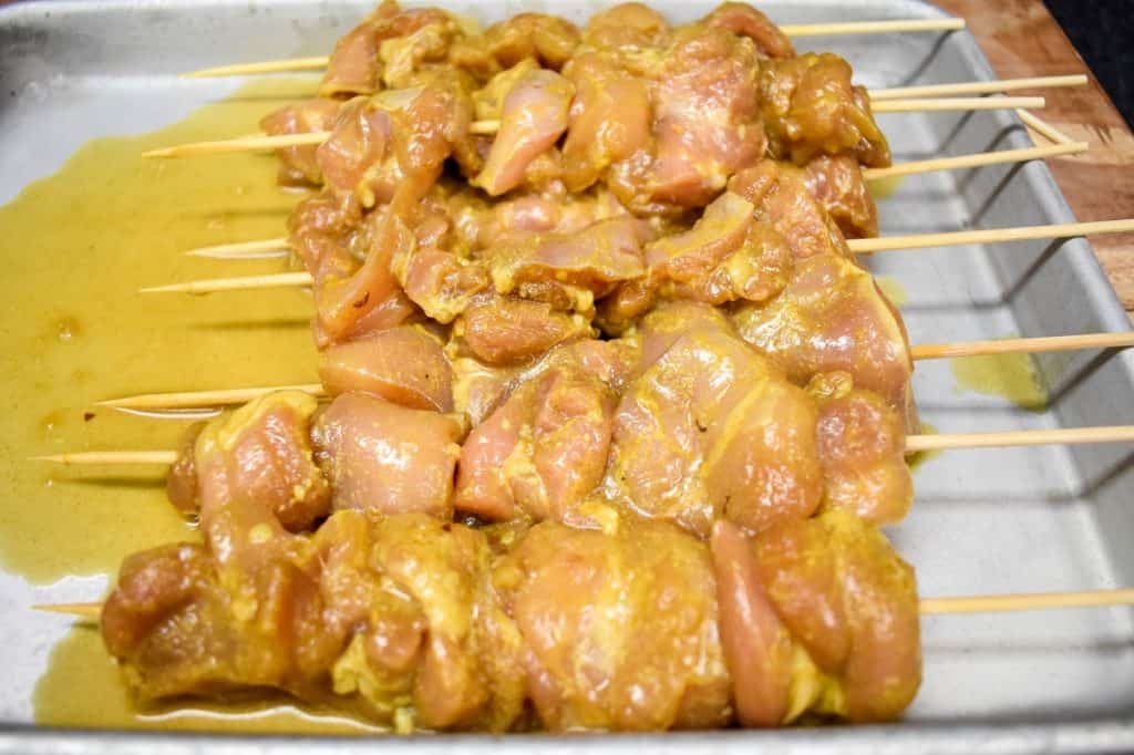 Eight chicken skewers before cooking, set on a metal sheet pan.