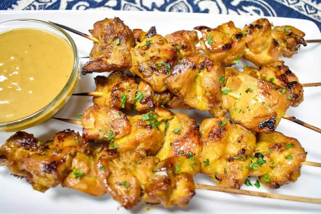 Chicken satay with peanut sauce served on a rectangular, white platter.