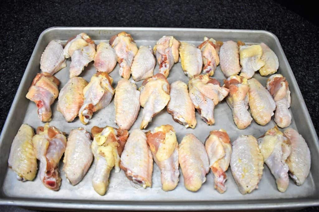 Raw chicken wings, drums and flats separated, arranged on a metal sheet pan.