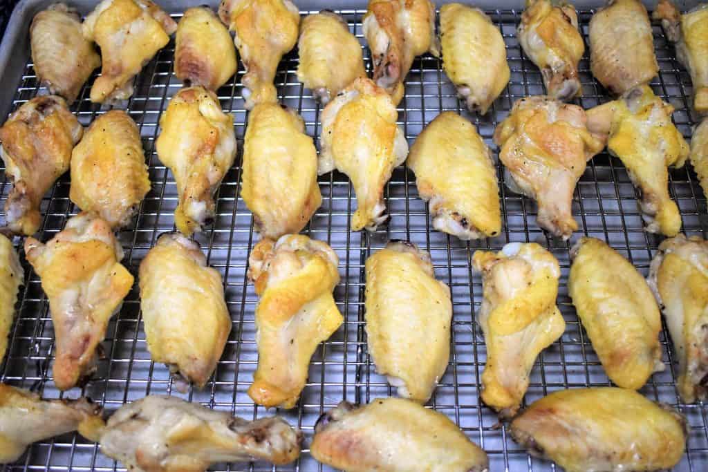 Chicken wings arranged on a sheet pan that's lined with a cooling rack.