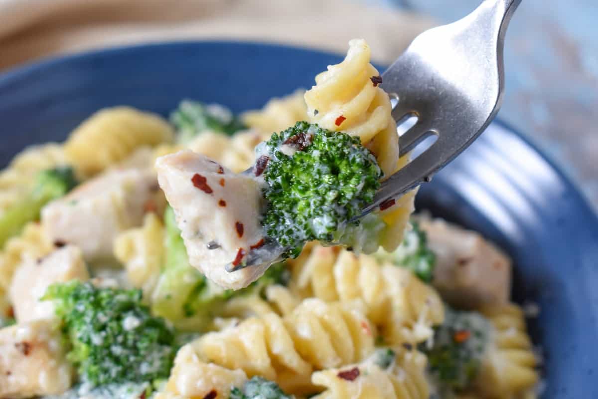 A bowl of the pasta and a fork holding up a piece of pasta, broccoli and chicken.