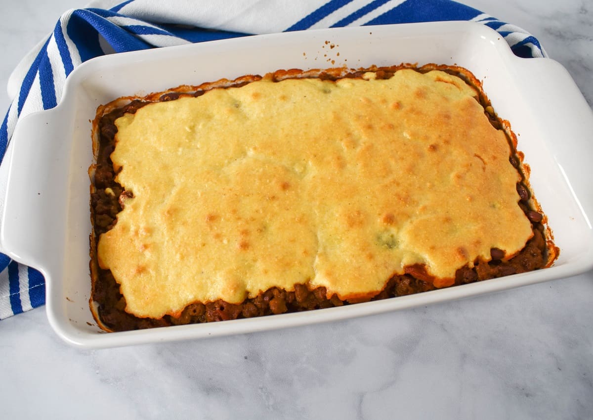 The baked chili cornbread casserole in a white dish with a blue and white striped kitchen towel behind it.
