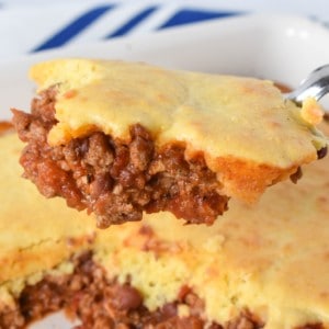 A piece of the chili cornbread casserole held up with a serving spoon over the casserole.