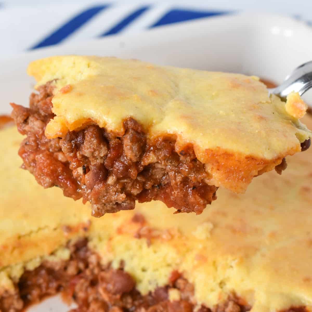 A piece of the chili cornbread casserole held up with a serving spoon over the casserole.