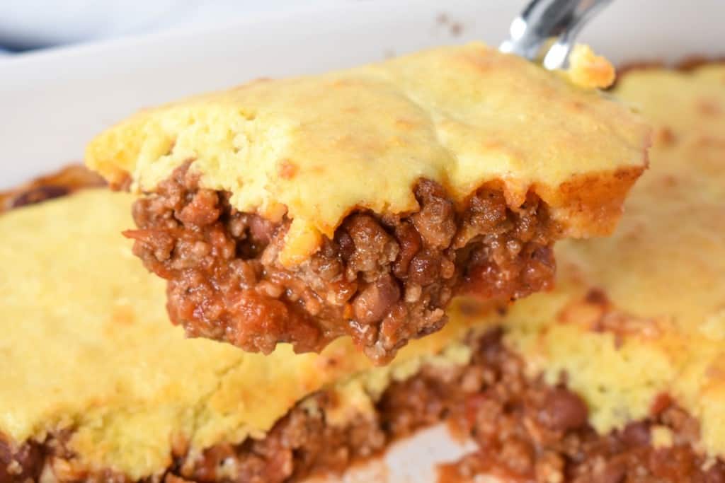 A piece of the chili cornbread casserole held up with a serving spoon over the casserole.