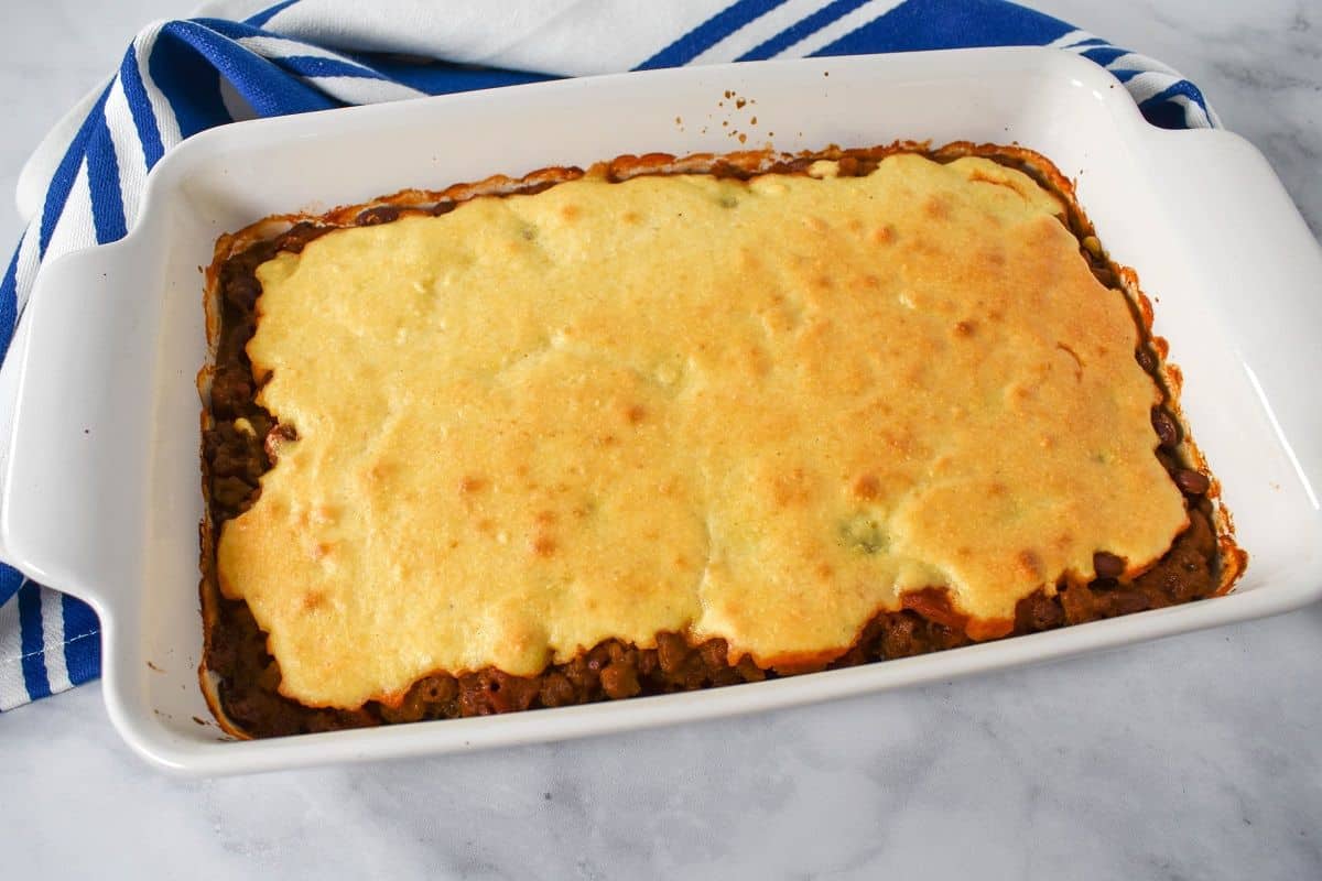 The baked chili cornbread casserole in a white dish with a blue and white striped kitchen towel behind it.