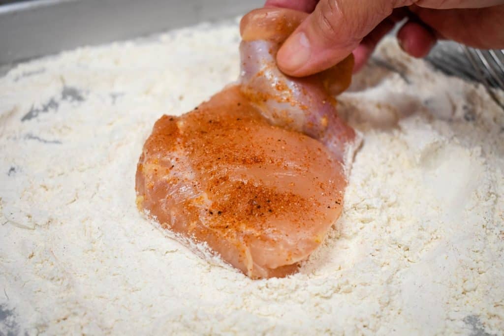 A seasoned chicken thigh being placed in flour.