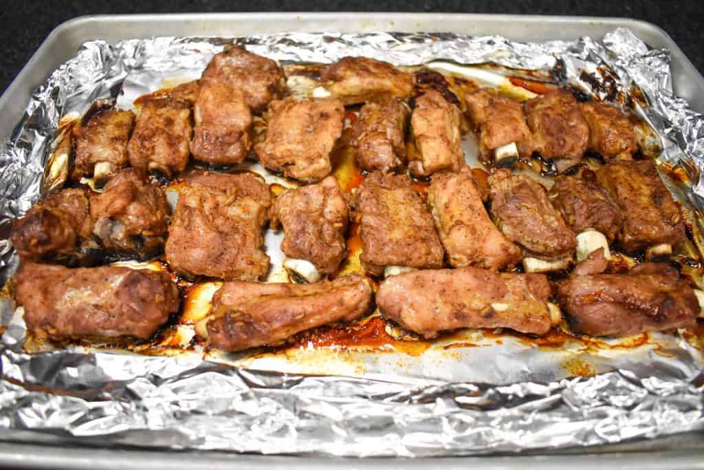 Cooked riblets on an aluminum foil lined baking sheet.