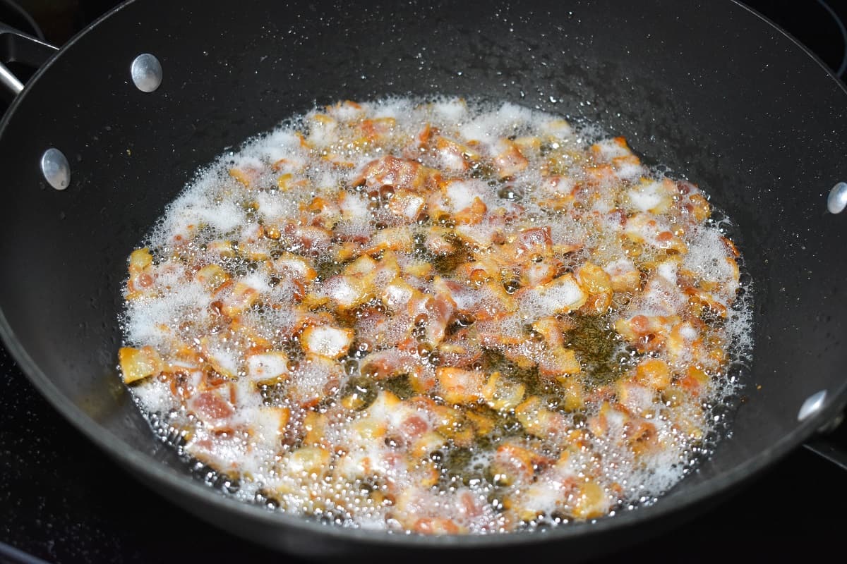 Chopped bacon frying in a large, black skillet.