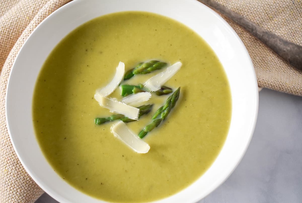 A close up image of the soup garnished with asparagus tips and parmesan cheese served in a white bowl.