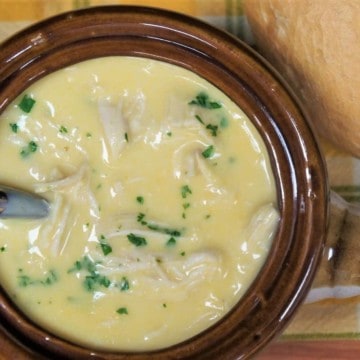 Cream of chicken soup served in a brown crock, garnished with parsley with a bread roll on the side