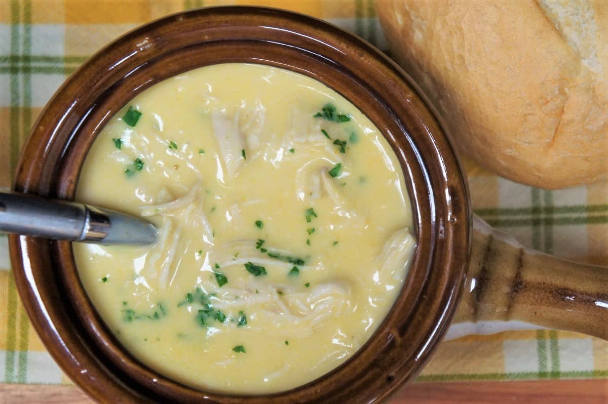 Cream of chicken soup served in a brown crock, garnished with parsley with a bread roll on the side